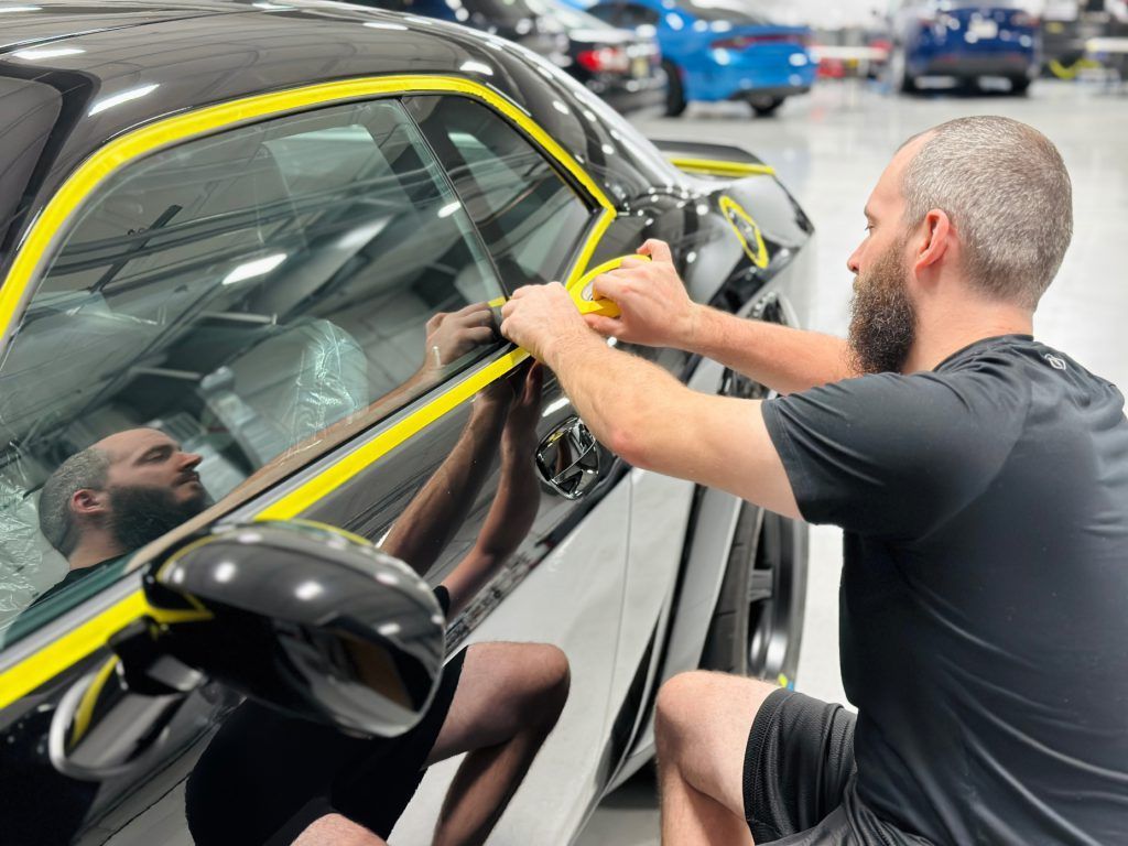A man is wrapping a car with yellow tape.
