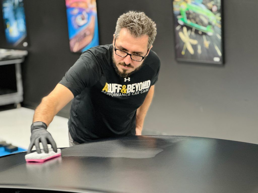 A man in a black shirt is cleaning a car with a sponge.