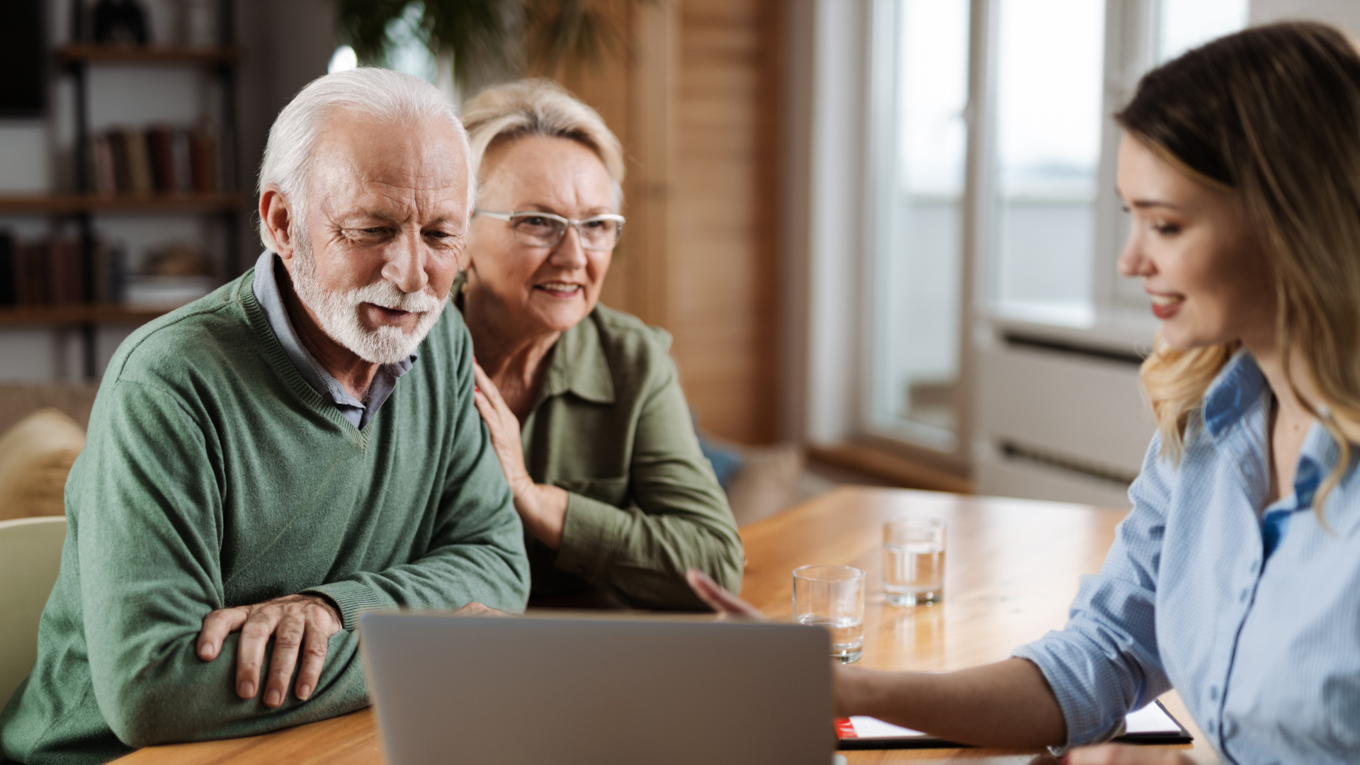 Senior couple looking at laptop with a younger woman in a home setting.