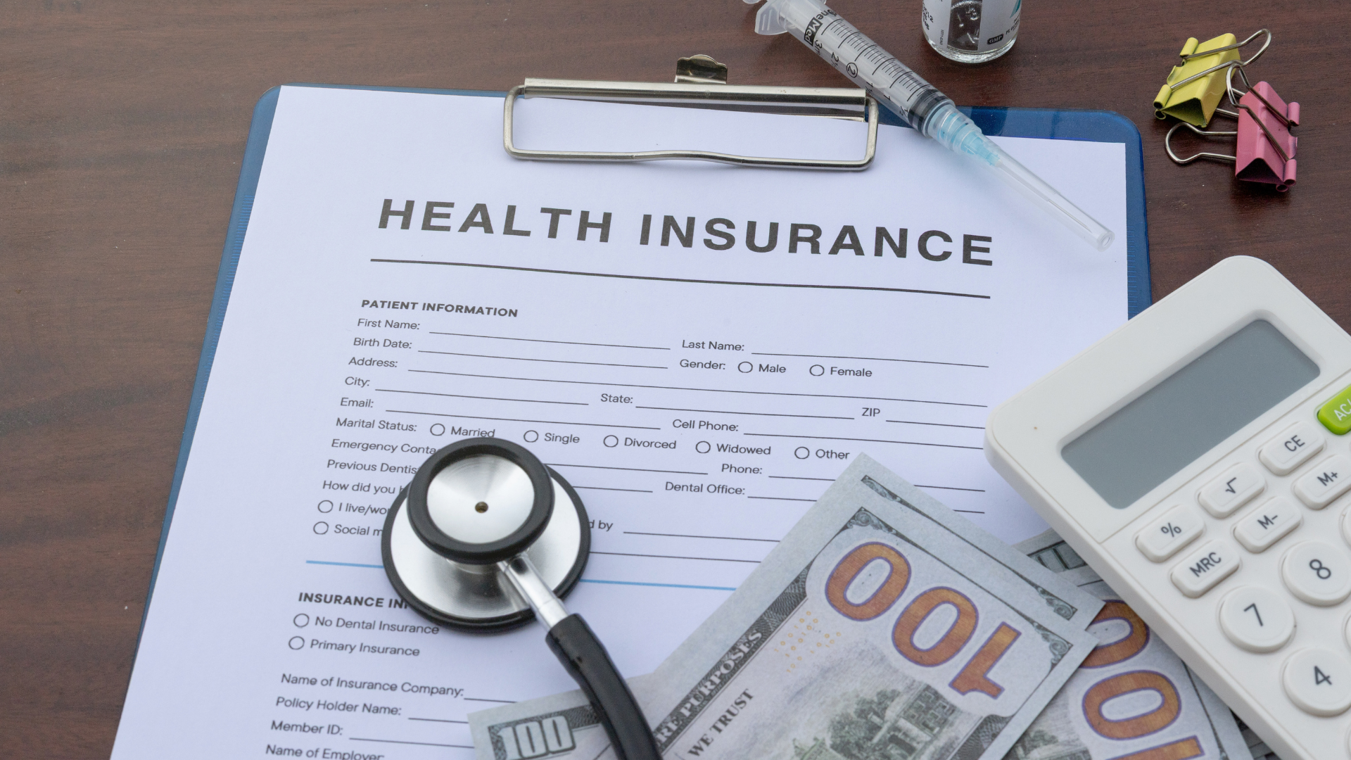 Health insurance paperwork with stethoscope, cash, calculator, and syringe.