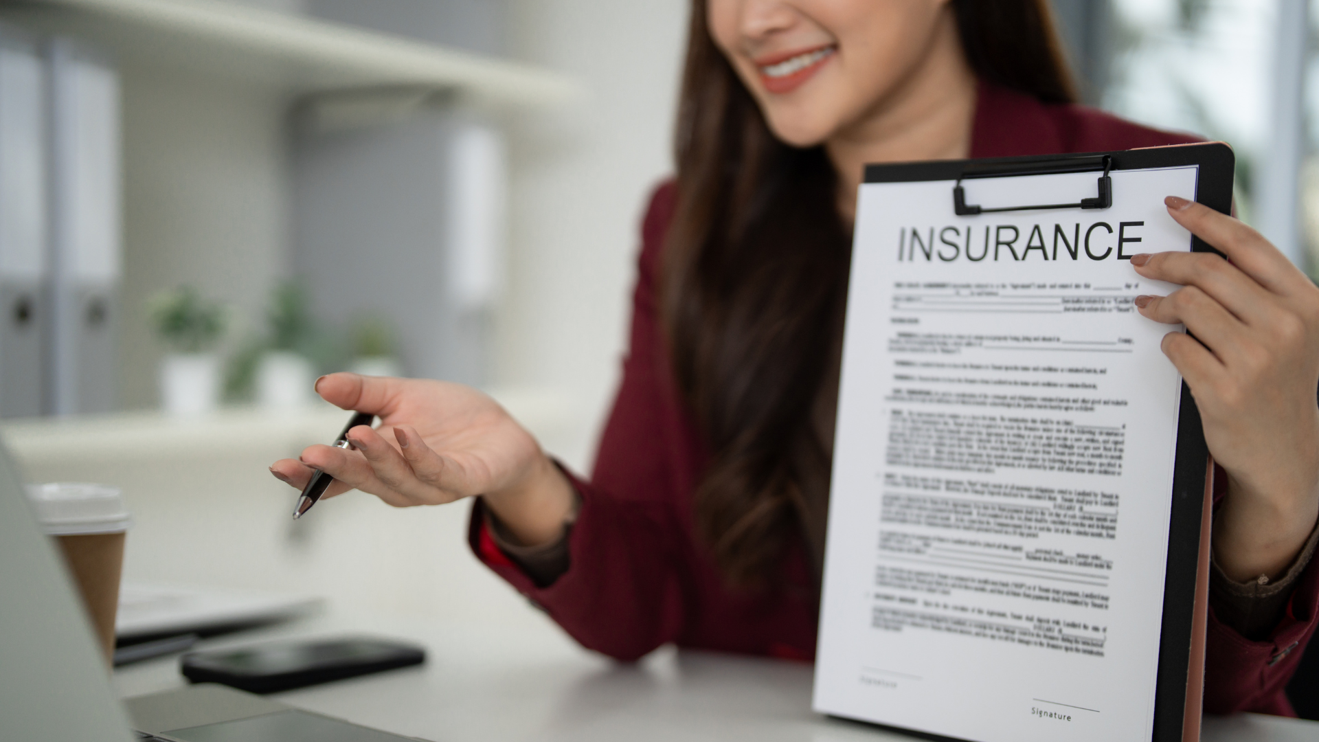 Woman in maroon blazer presents an insurance form during a video call, smiling.