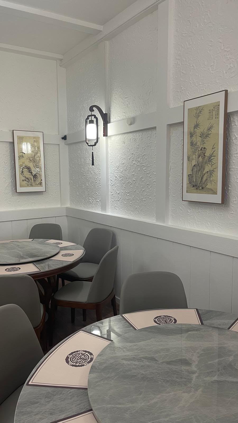 Gemütliche Café-Ecke mit runden Tischen, grauen Stühlen, Wandkunst und sanft strukturierten weißen Wänden.