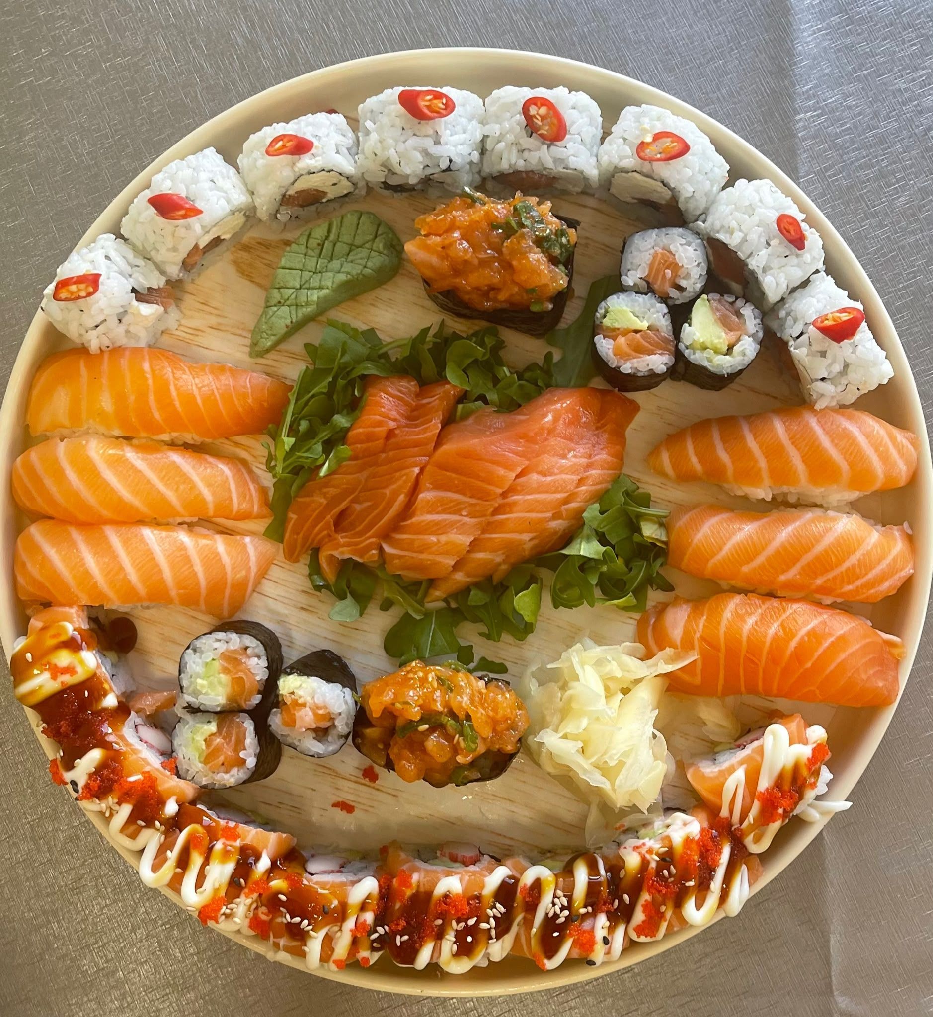 Verschiedene Sushi-Rollen und Nigiri, angerichtet auf einem runden weißen Teller mit Saucen und Garnitur
