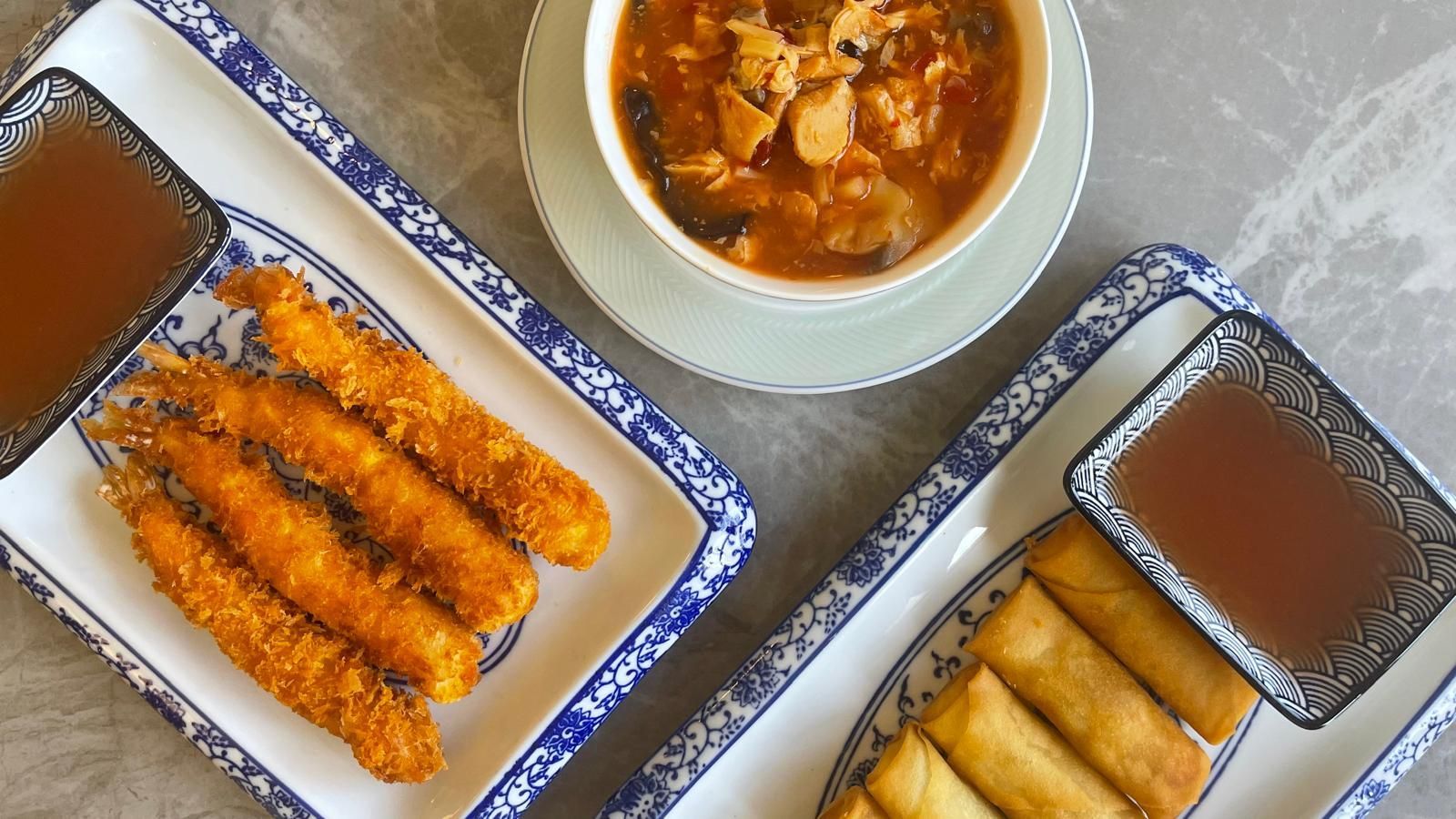 Frittierte Vorspeisen und Dips auf gemusterten Tellern, mit einer Schüssel Suppe in der Mitte.