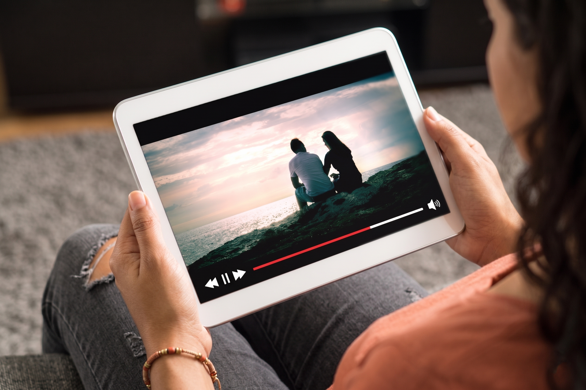 Person holding a tablet streaming a video of two people sitting on a beach at sunset