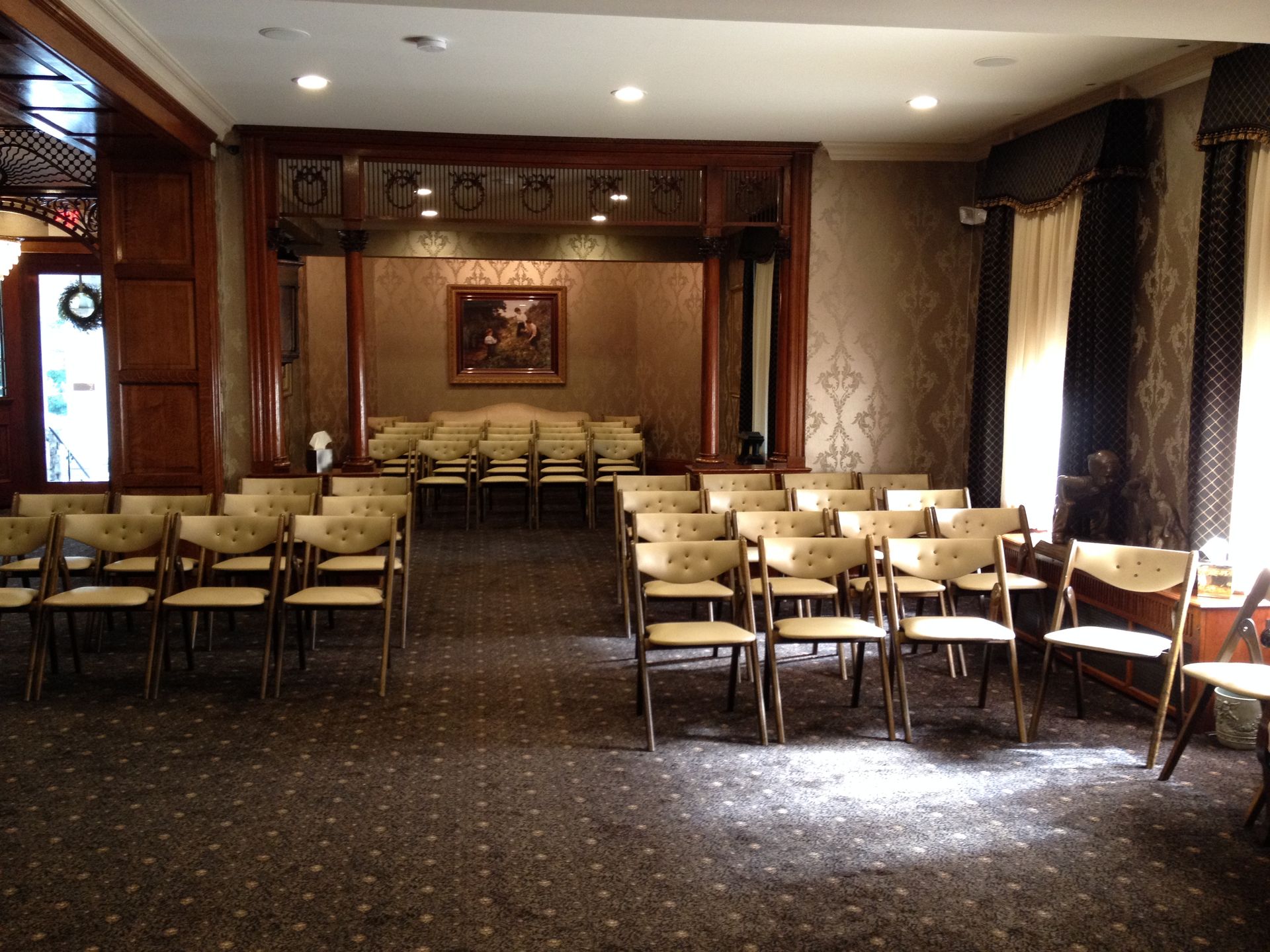 Empty banquet hall with rows of chairs and tables, warm lighting, and a framed picture on the back wall