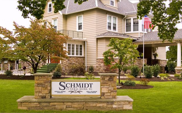 Schmidt sign in front of a beige house with green lawn and autumn trees