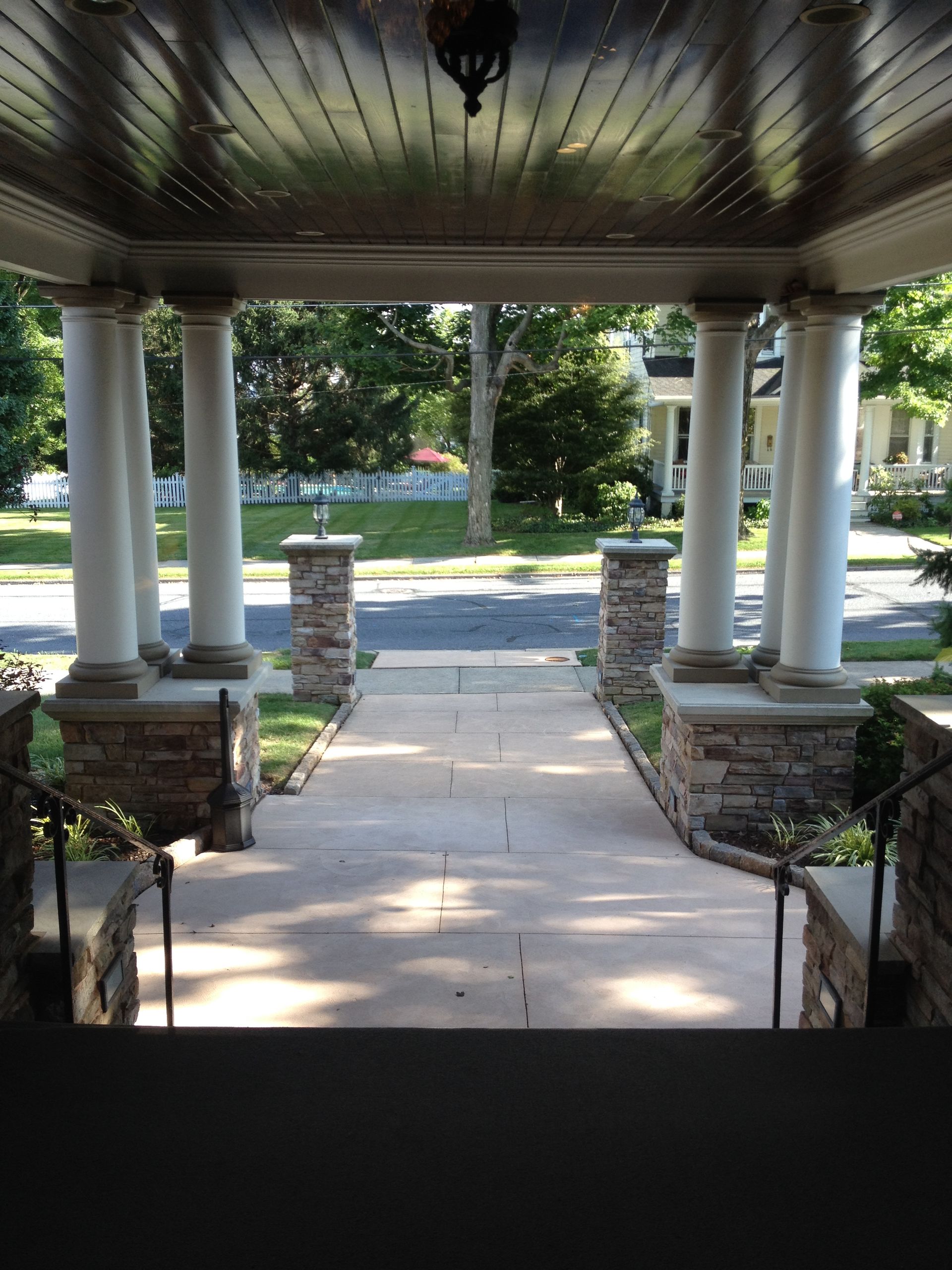 Covered front porch with white columns overlooking a tree-lined yard and street.