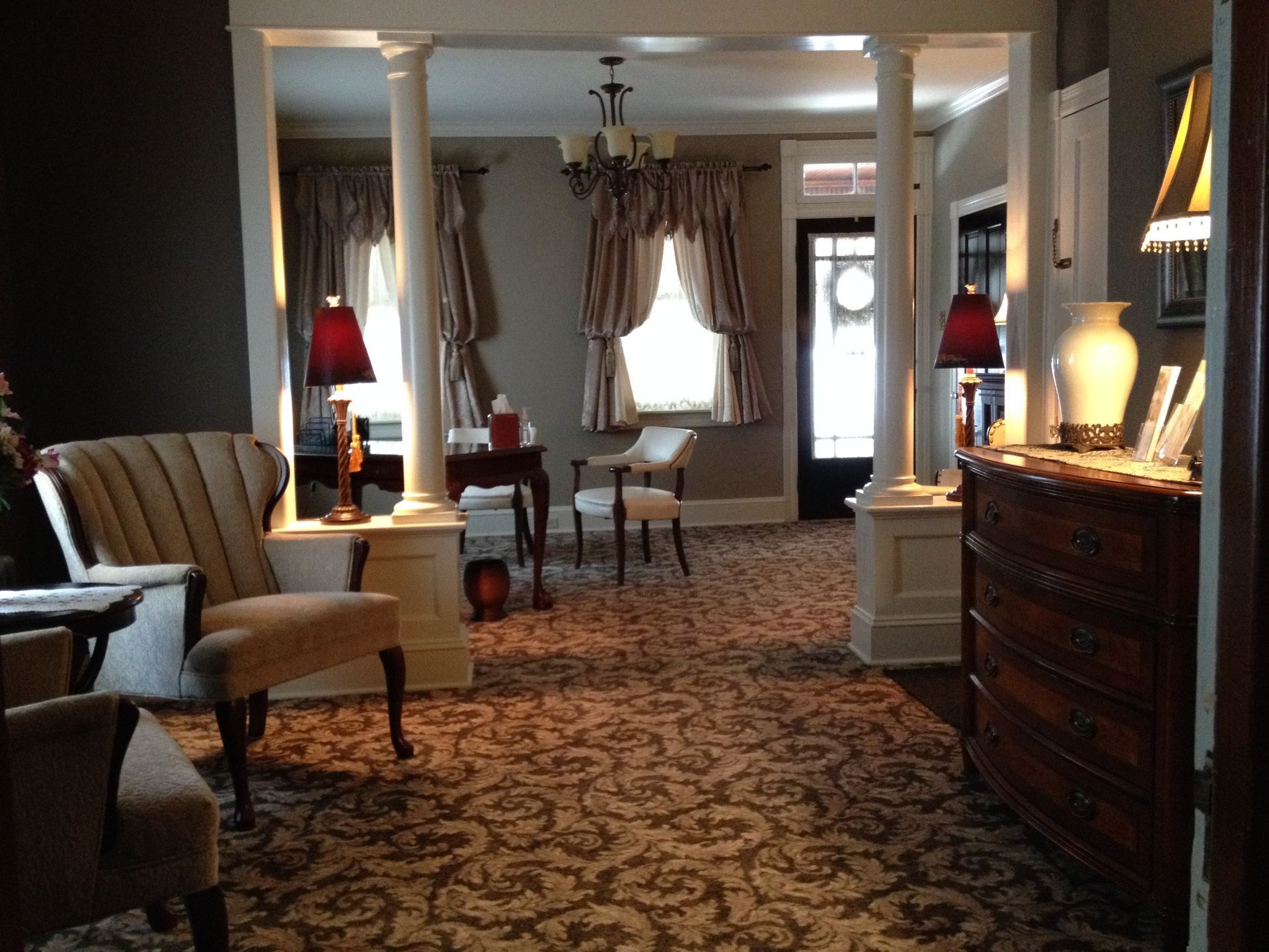 Elegant living room with patterned carpet, white columns, and striped chairs under warm lamplight