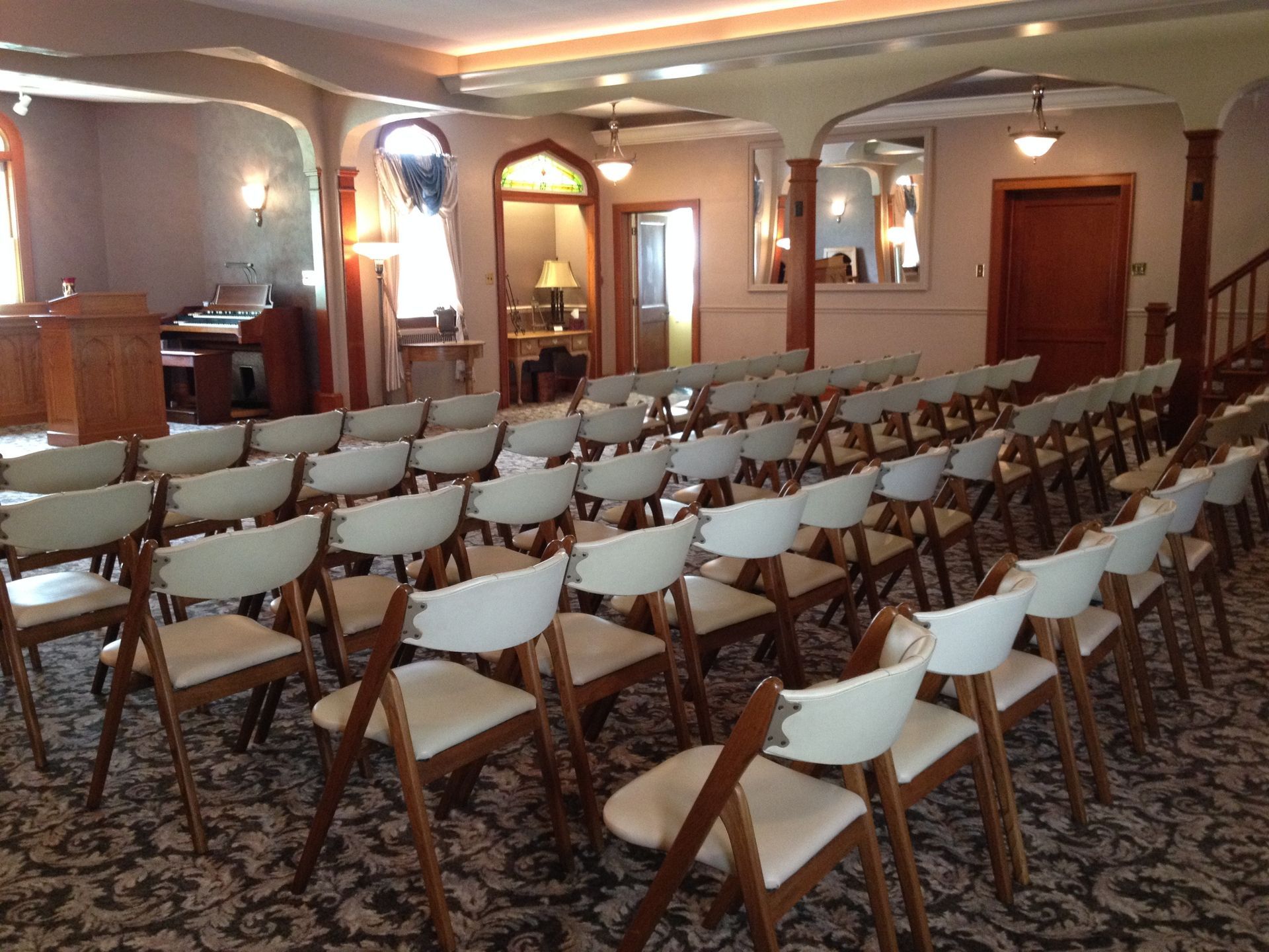 Rows of empty white chairs set up in a warmly lit banquet hall with carpeted floor.