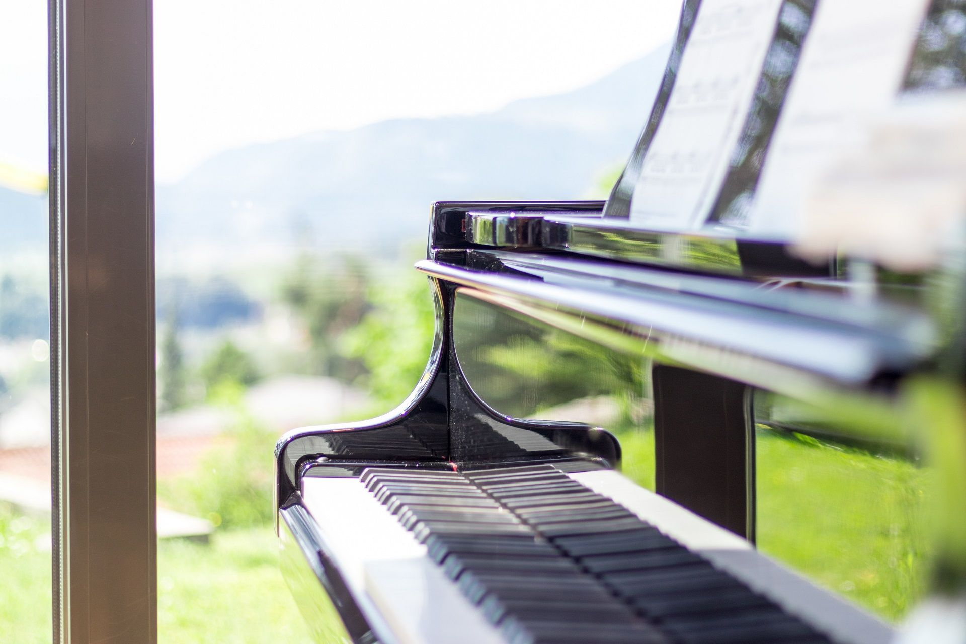 Close-up of a grand piano keyboard by a bright window with green countryside outside