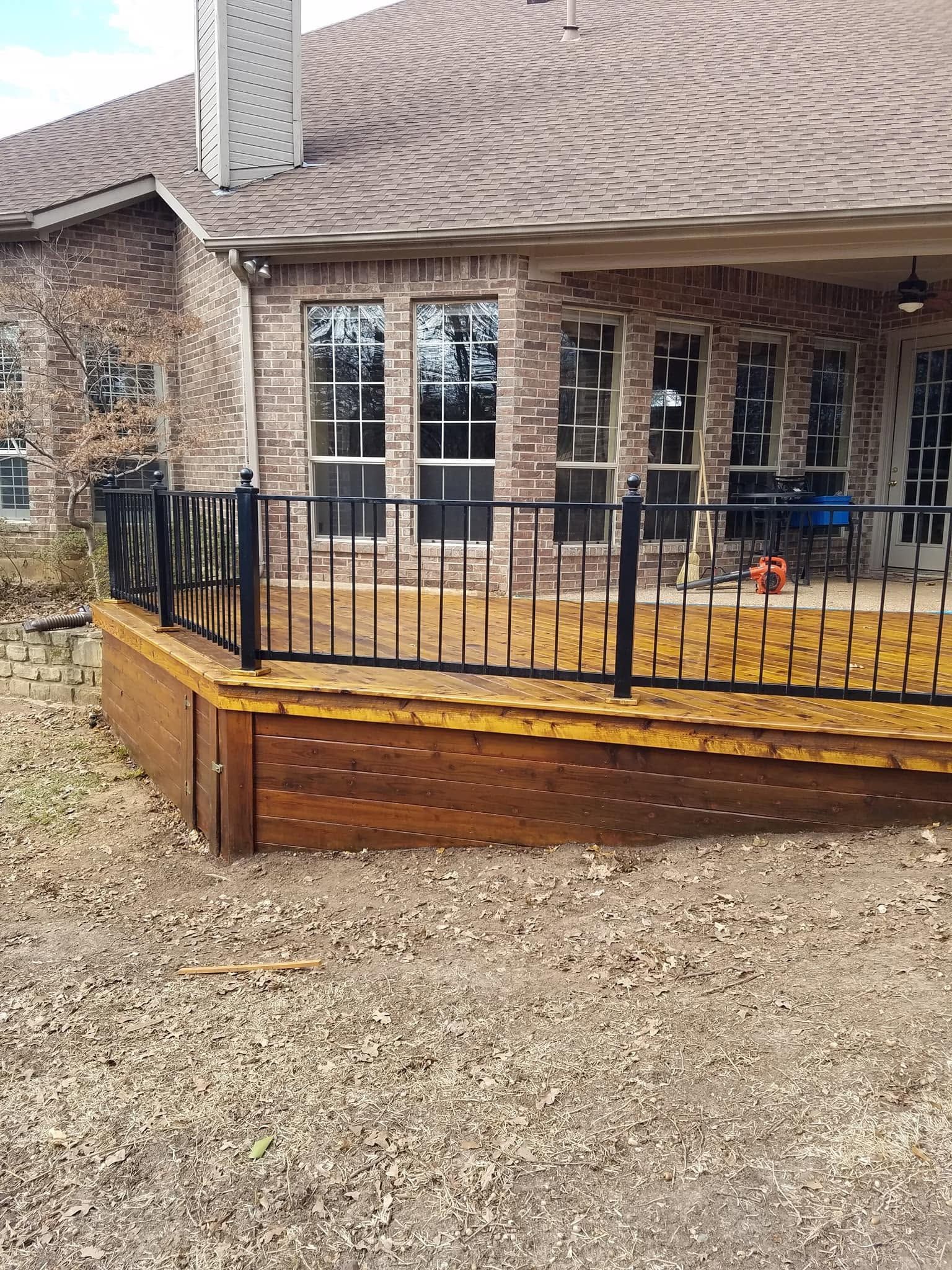Brick house porch with black railing, yellow planter box, and gravel driveway