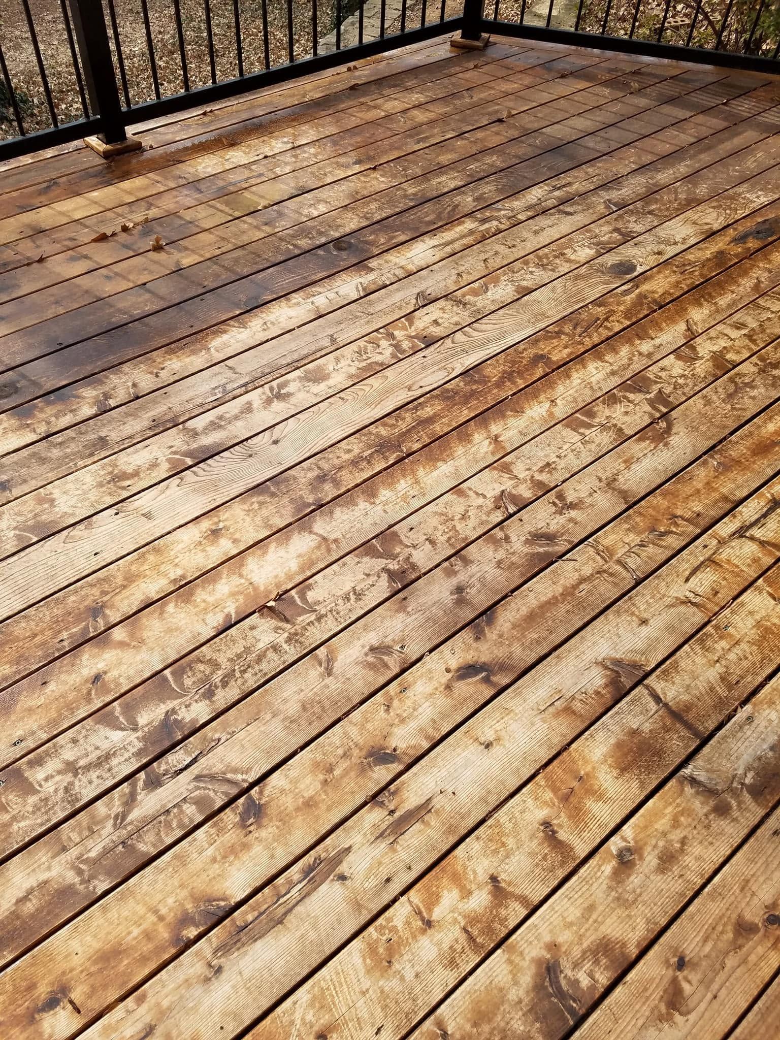 Weathered wooden deck boards in sunlight, with a black railing along the top edge.