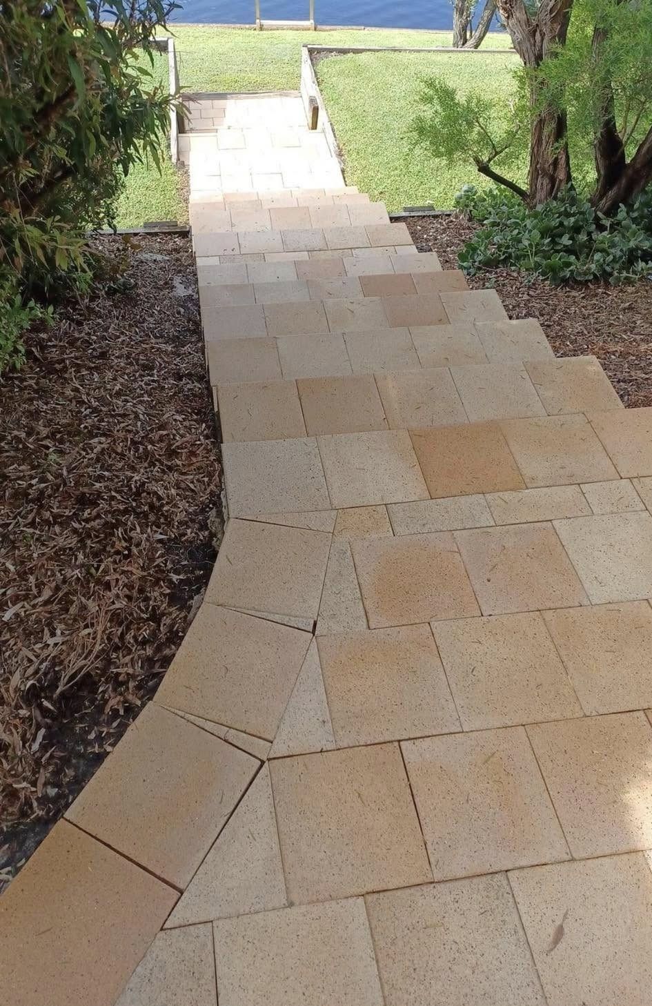 Stone walkway leading through a garden toward a bright grassy area beyond.
