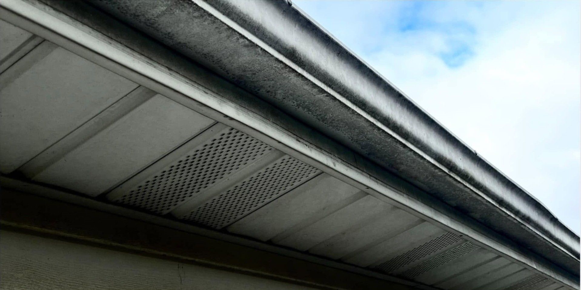 Close-up of a house roof eave with white soffit and gutter against a blue sky