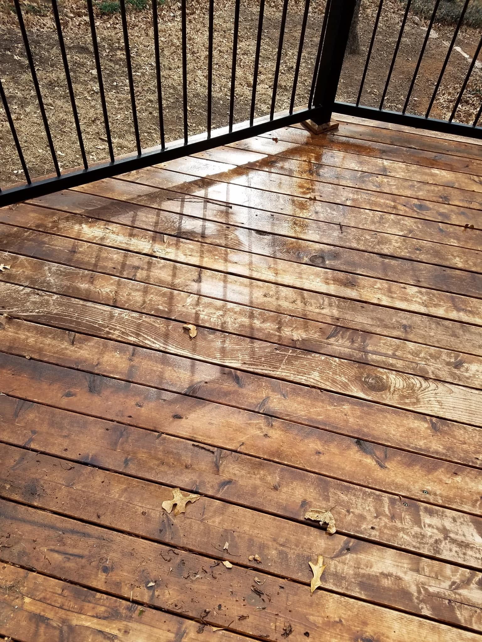 Wet wooden deck with black railing and sunlight reflections