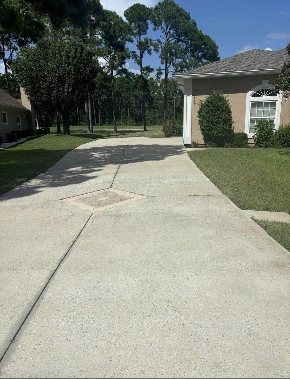 Concrete driveway leading to a suburban house with trees and lawn on a sunny day