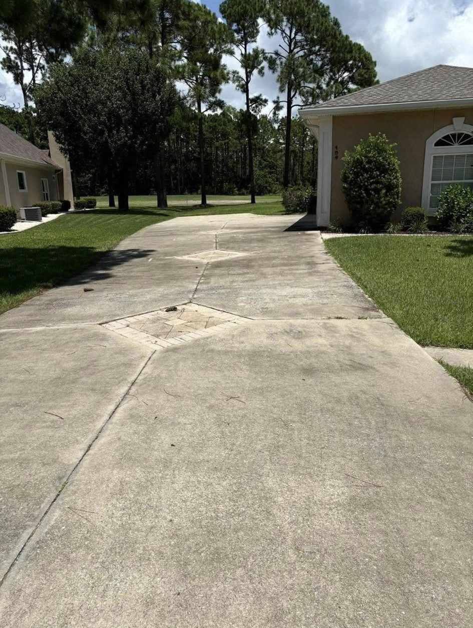 Concrete driveway leading to a house with trees and lawn on a sunny day