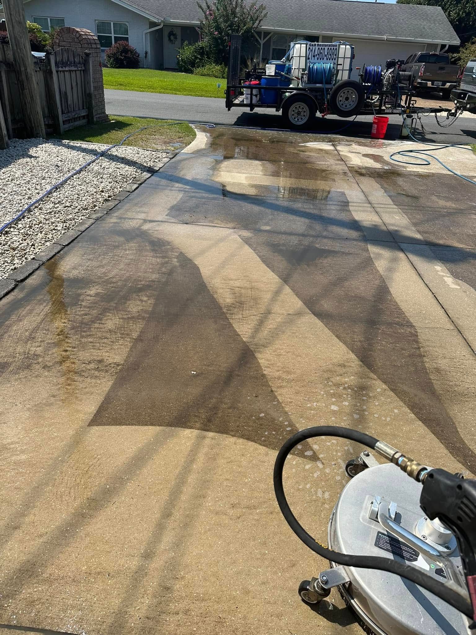 Driveway being pressure washed, with a cleaning truck and hose in the background.