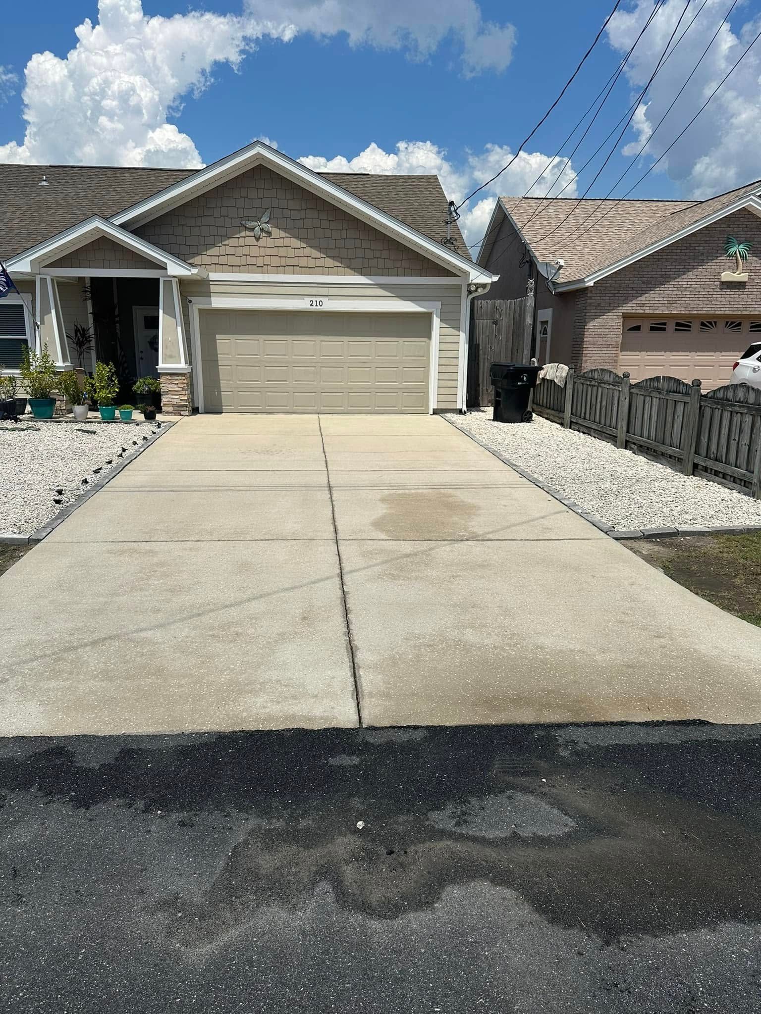 Suburban house with two-car garage, wide concrete driveway, and clear blue sky with clouds.