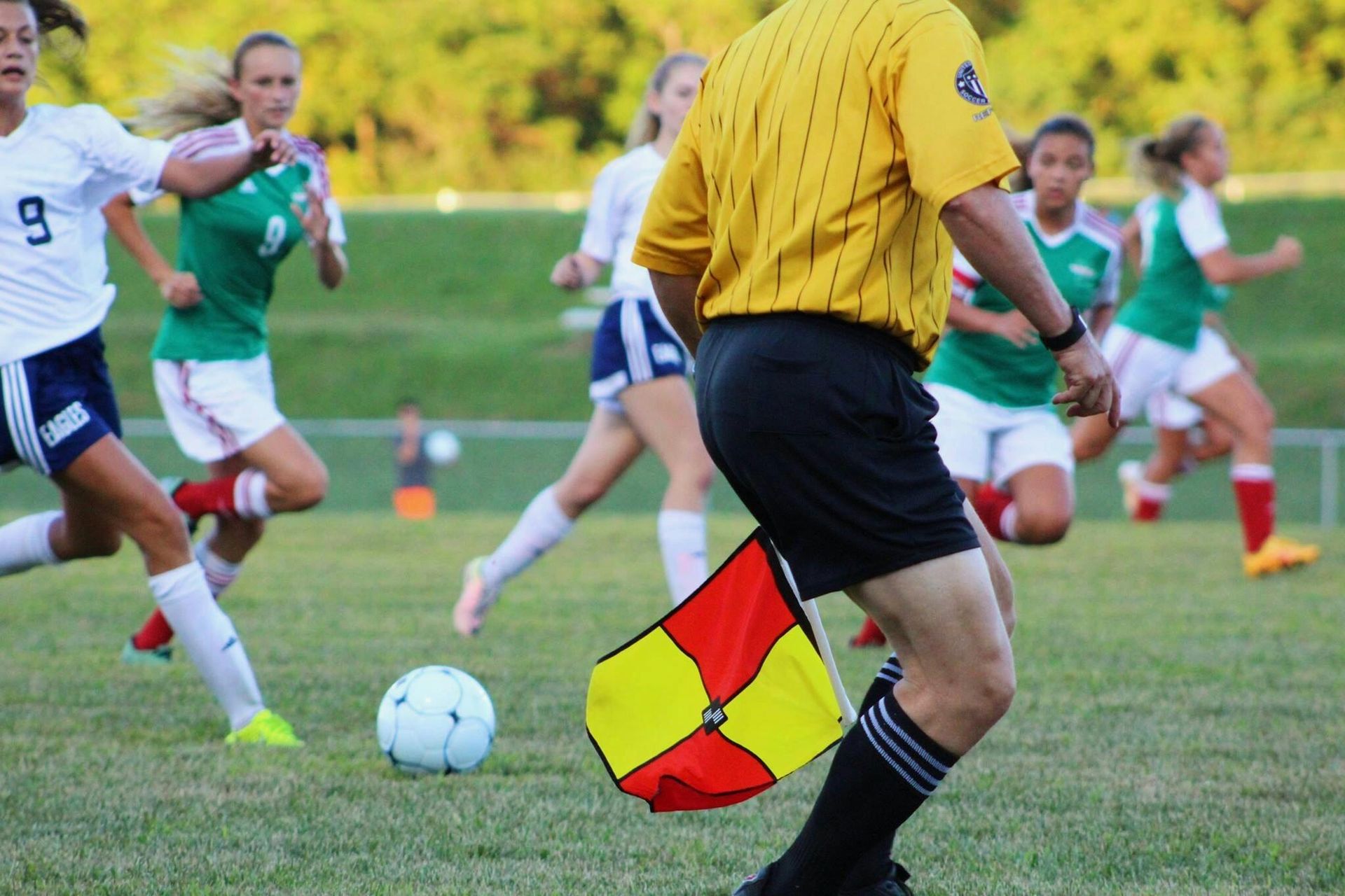 A referee is holding a red and yellow flag while playing soccer.