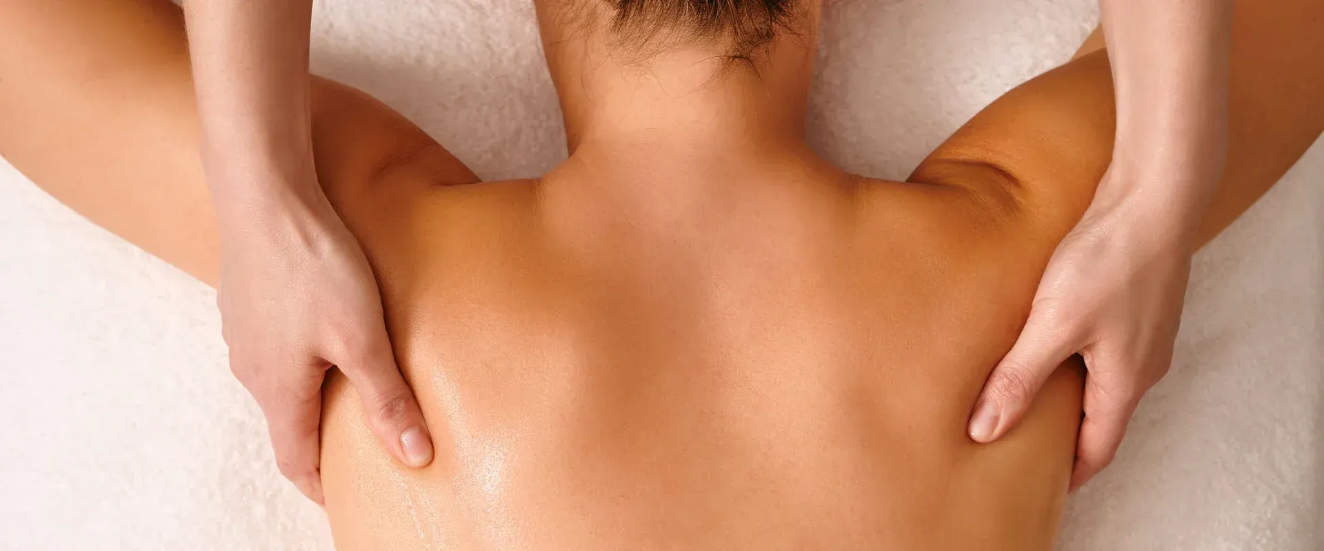Hands massaging a person's bare upper back and shoulders on a white towel-covered surface