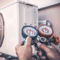 Les mains d'un technicien utilisant un manomètre pour vérifier la pression du réfrigérant sur une unité de climatisation extérieure.
