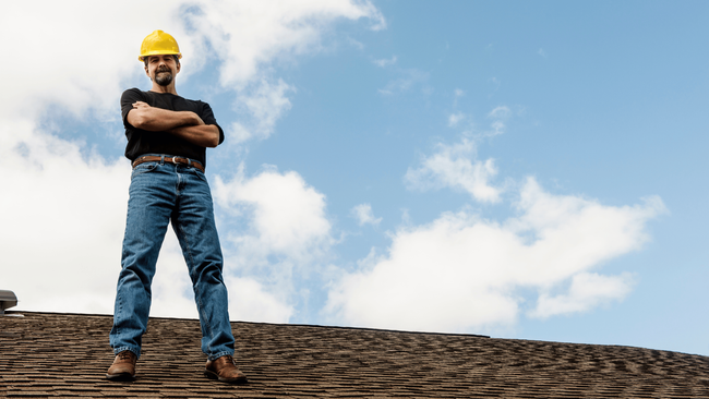 A man wearing a hard hat is standing on top of a roof.