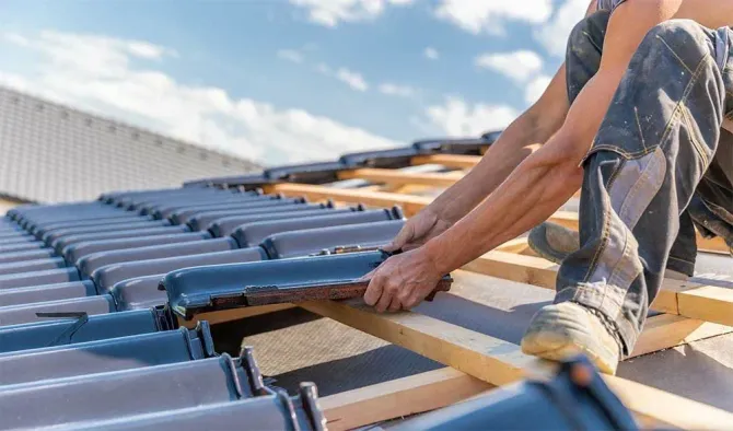 A man is installing tiles on the roof of a building.