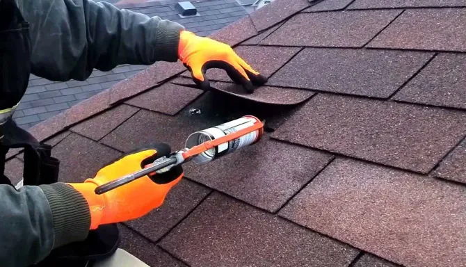 A man wearing orange gloves is working on a roof.