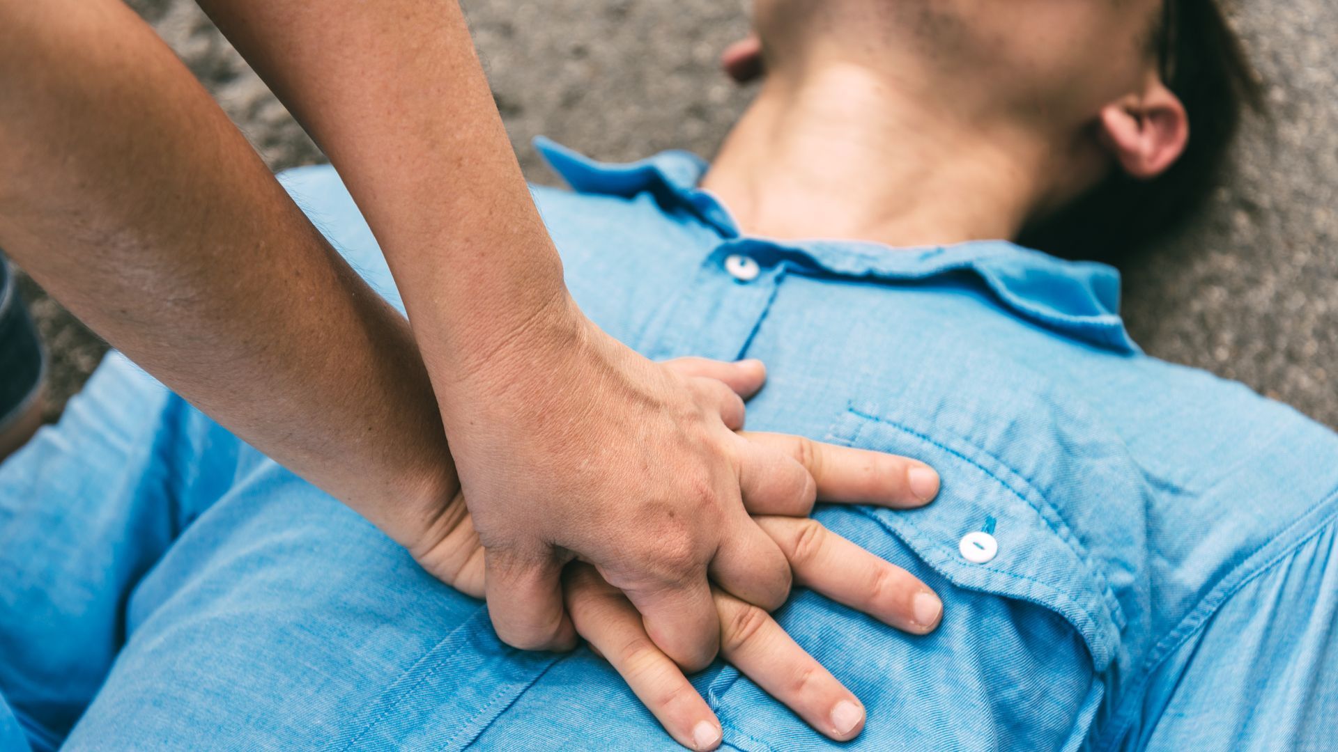 Hands performing chest compressions on a person wearing a blue shirt to provide CPR.