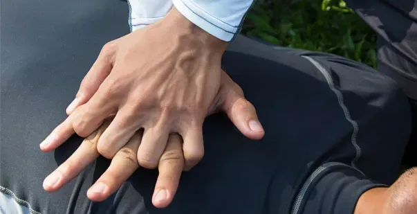 Hands are interlocked and positioned on a person's chest to perform CPR.