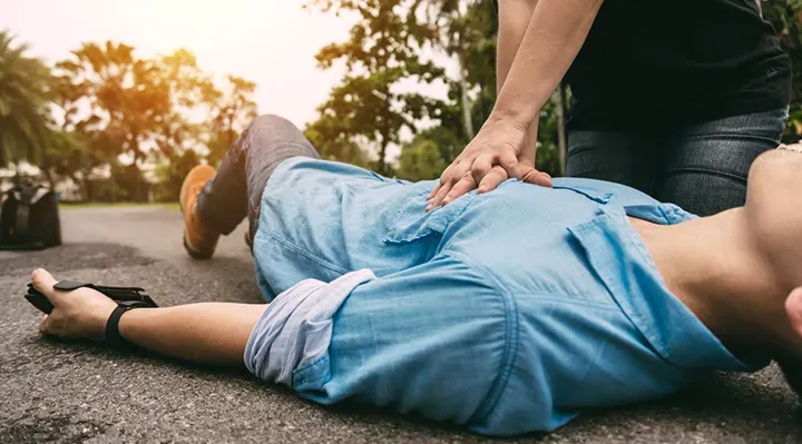 A person performs CPR on another individual lying on the ground outdoors.