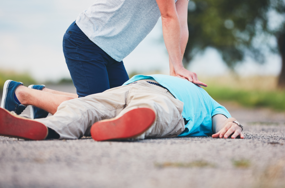 A person kneeling on a road while performing chest compressions on an individual lying on the ground.