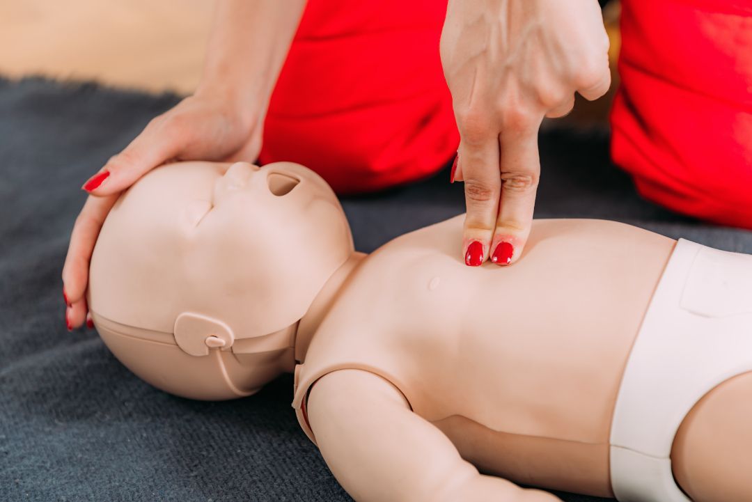 A person performs infant CPR chest compressions on a training mannequin using two fingers.