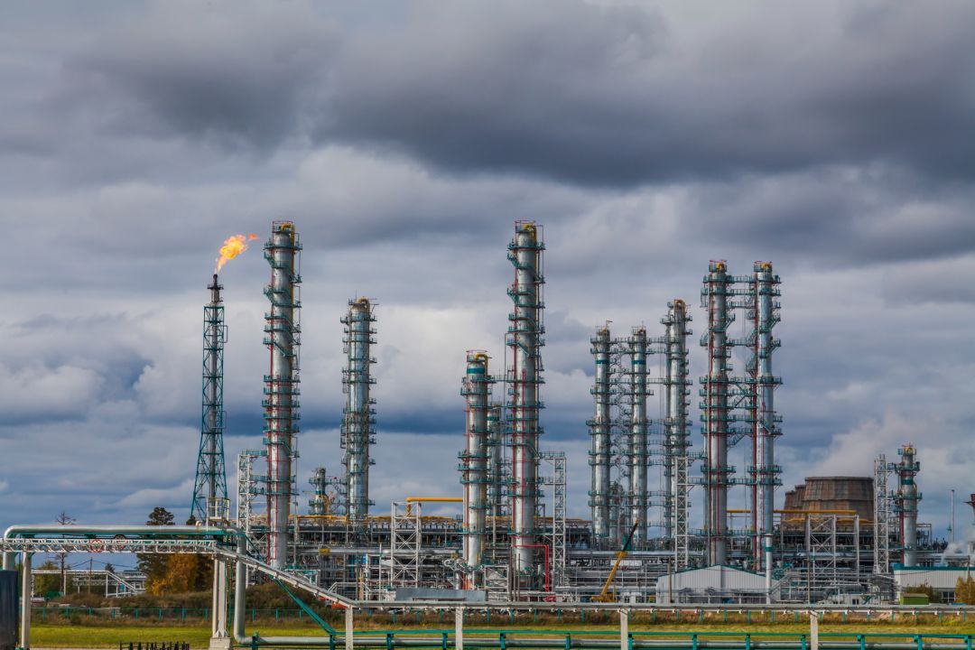 Oil refinery with tall distillation towers and a flare stack under dark storm clouds