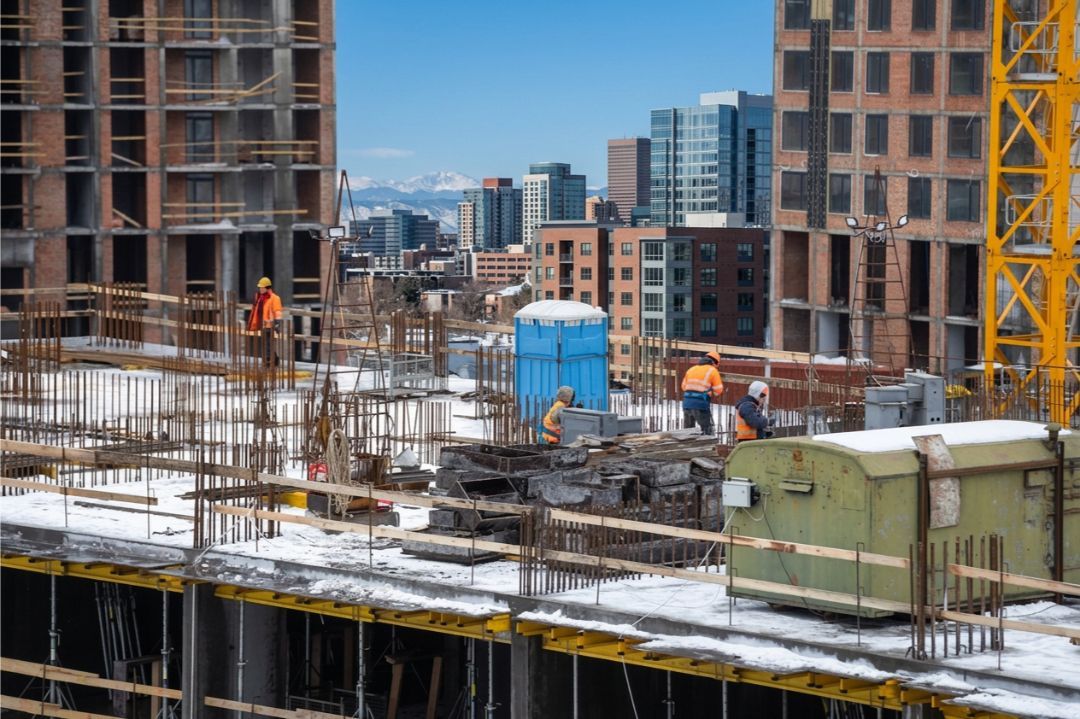Winter construction site in Colorado USA with workers and modern apartment building under clear high-altitude sky