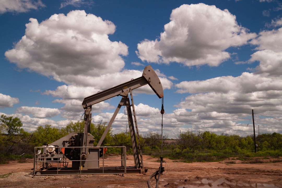 Oil pumpjack in a muddy field under a cloudy sky.