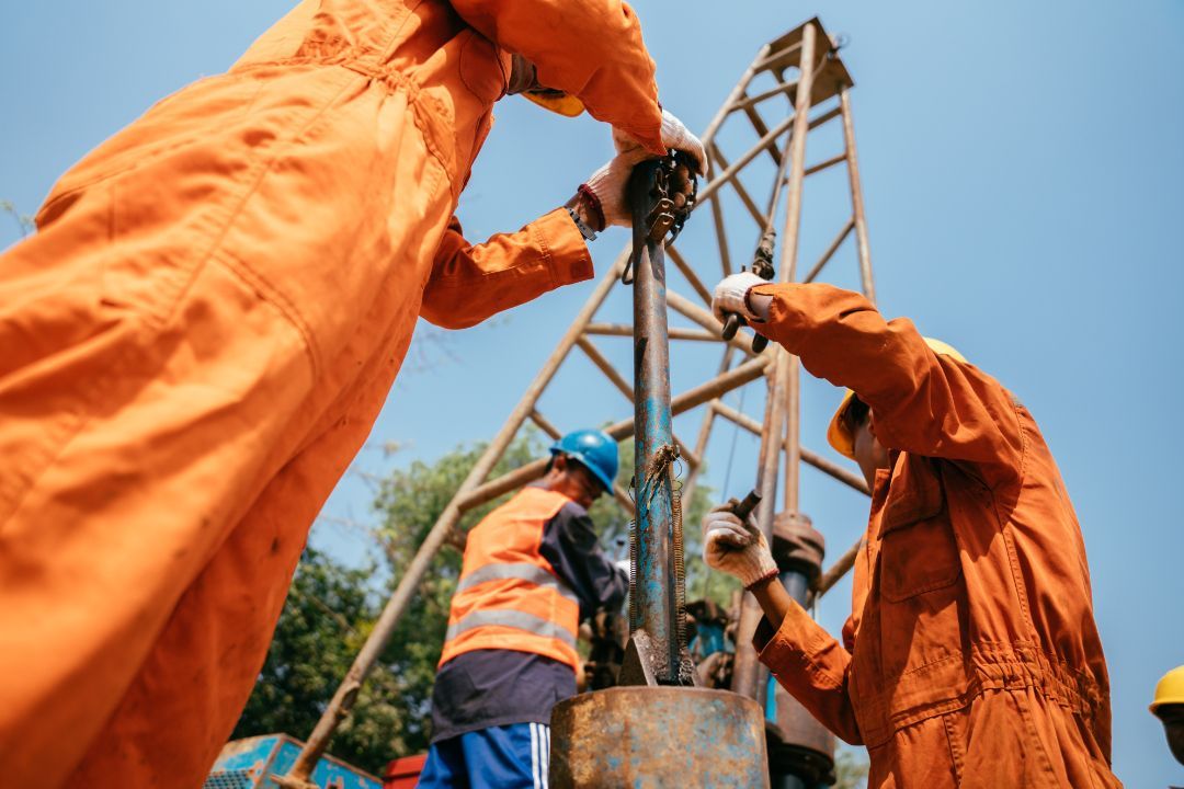 Workers in orange coveralls and hard hats assembling a metal tower at a construction site.