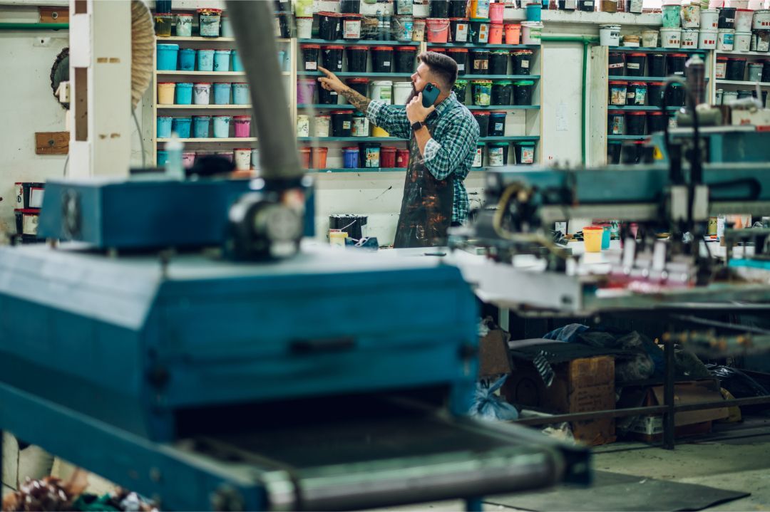 Person on a phone in a busy workshop with shelves and machinery in the background