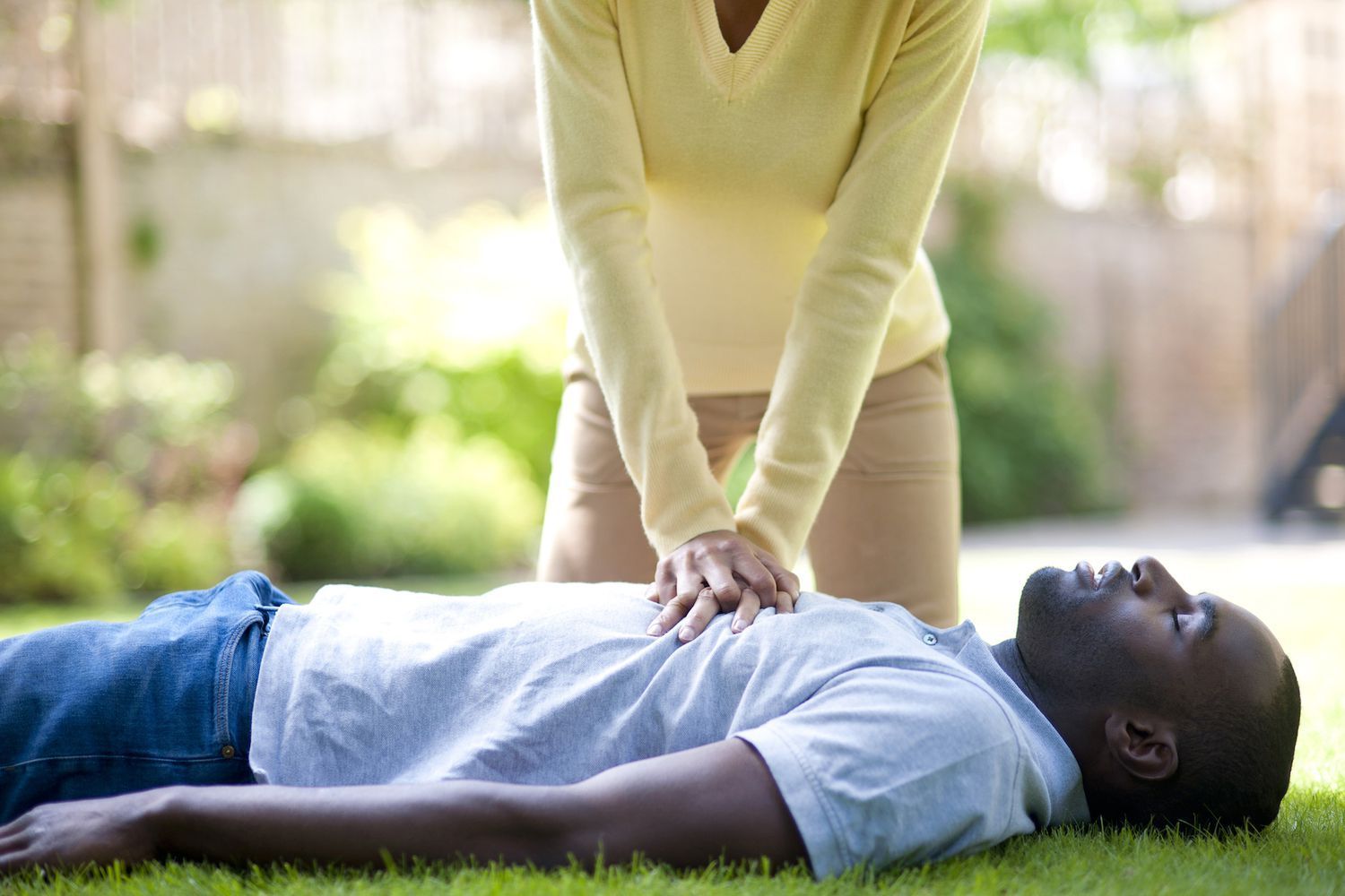 A person performs hands-only CPR on a person lying on their back on the grass.