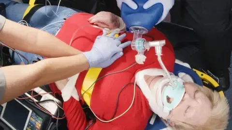Emergency medical responders perform CPR and provide ventilation support to a person on a stretcher.