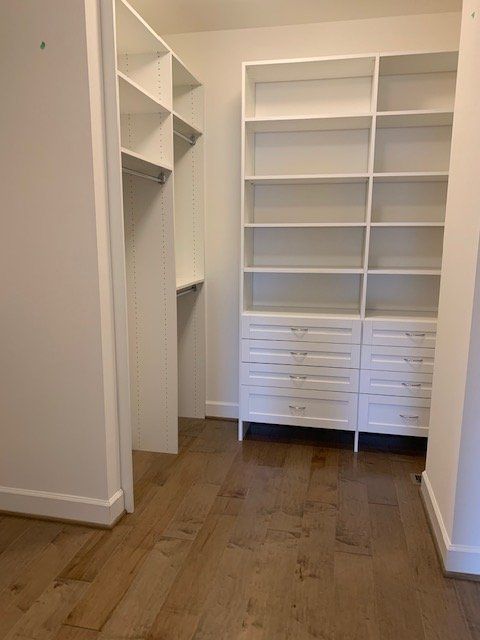 A walk-in closet featuring white wooden shelving, open hanging rods, and a lower section of built-in drawers.