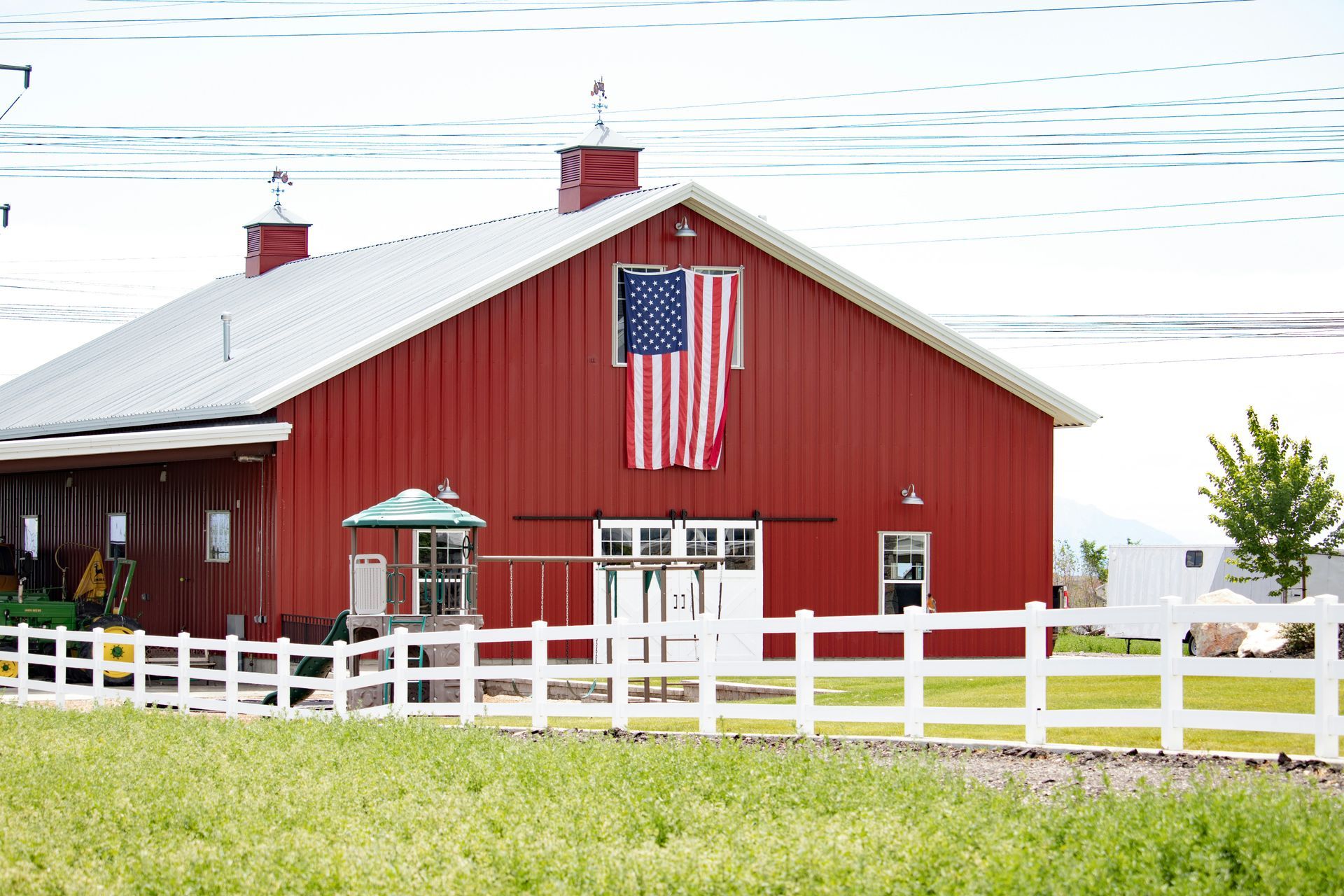 Red barn with an American flag, white fence, and green field under a bright sky