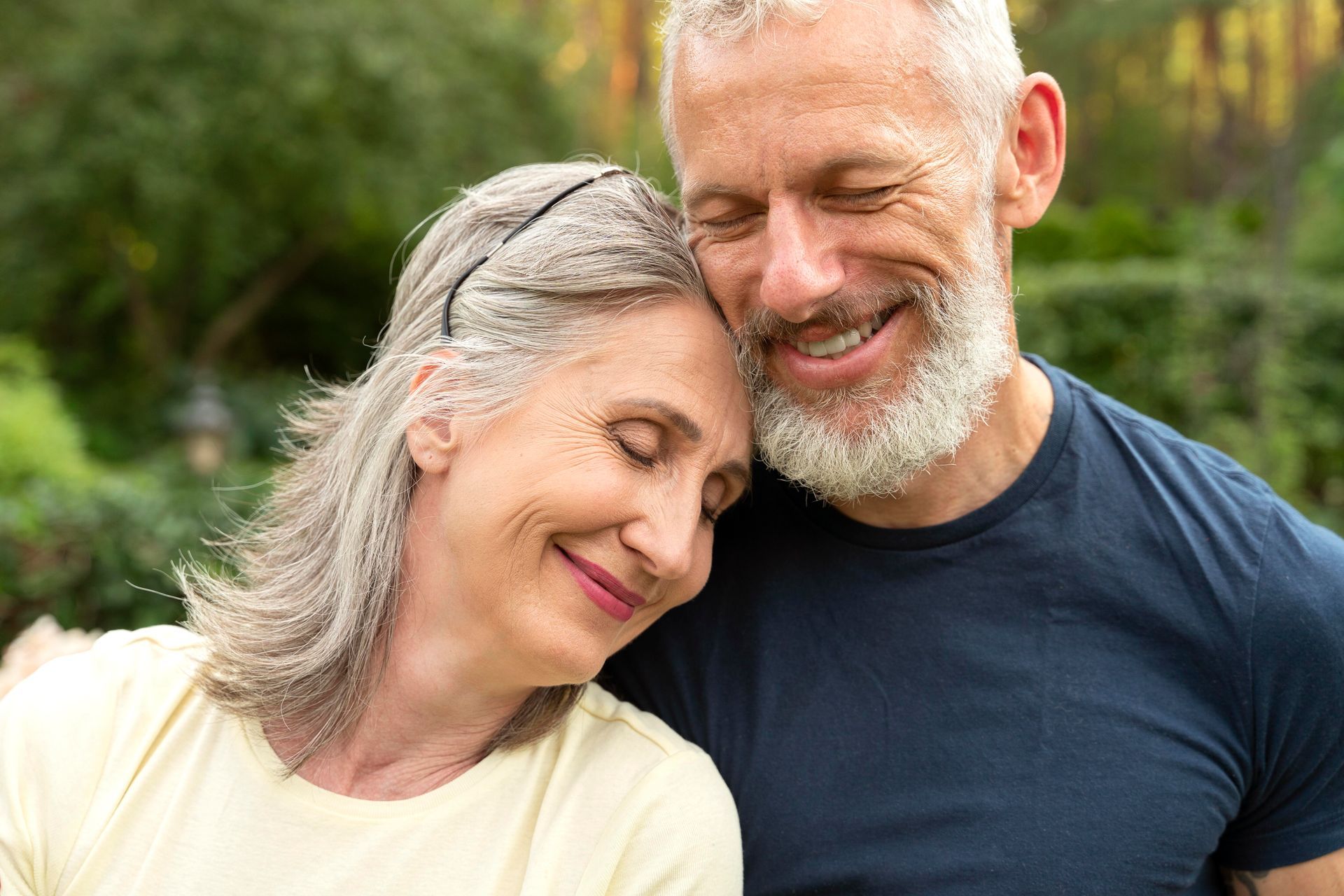 Two smiling people leaning their heads together outdoors in a leafy garden