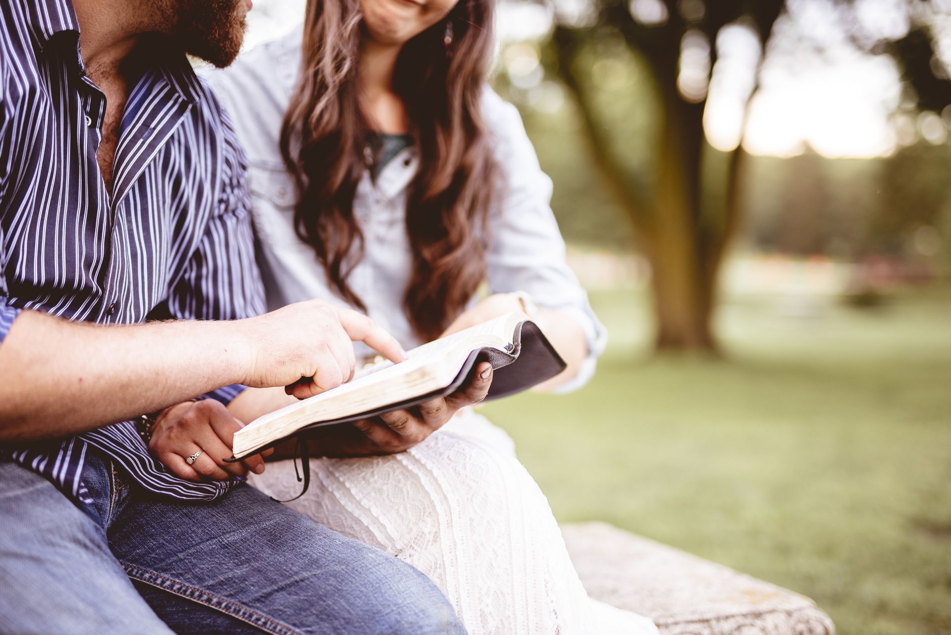 Two people sitting outdoors, reading from an open book on a bench