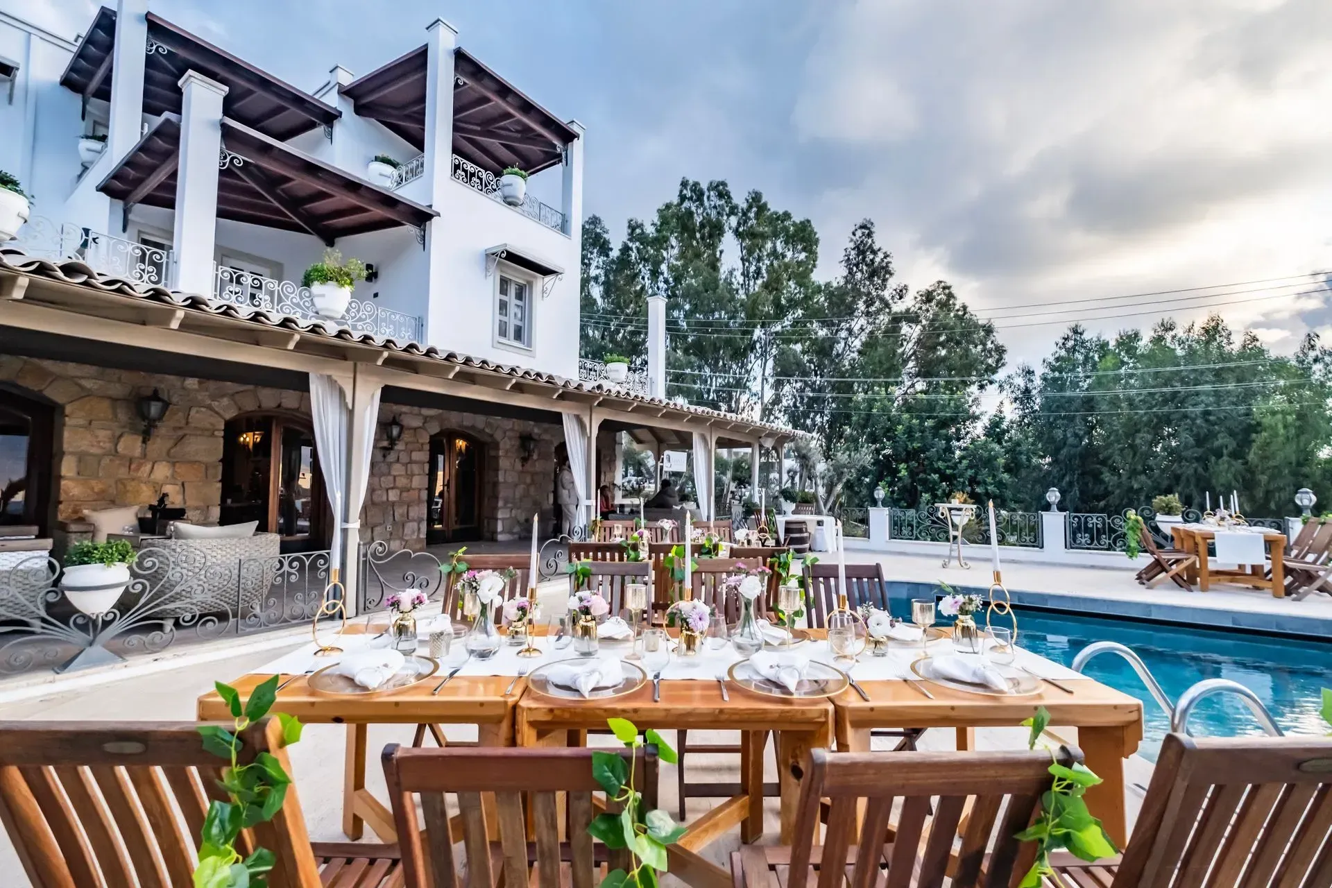 Manzara Boutique Hotel | Poolside dining terrace with wooden tables, white villa, and blue swimming pool at sunset