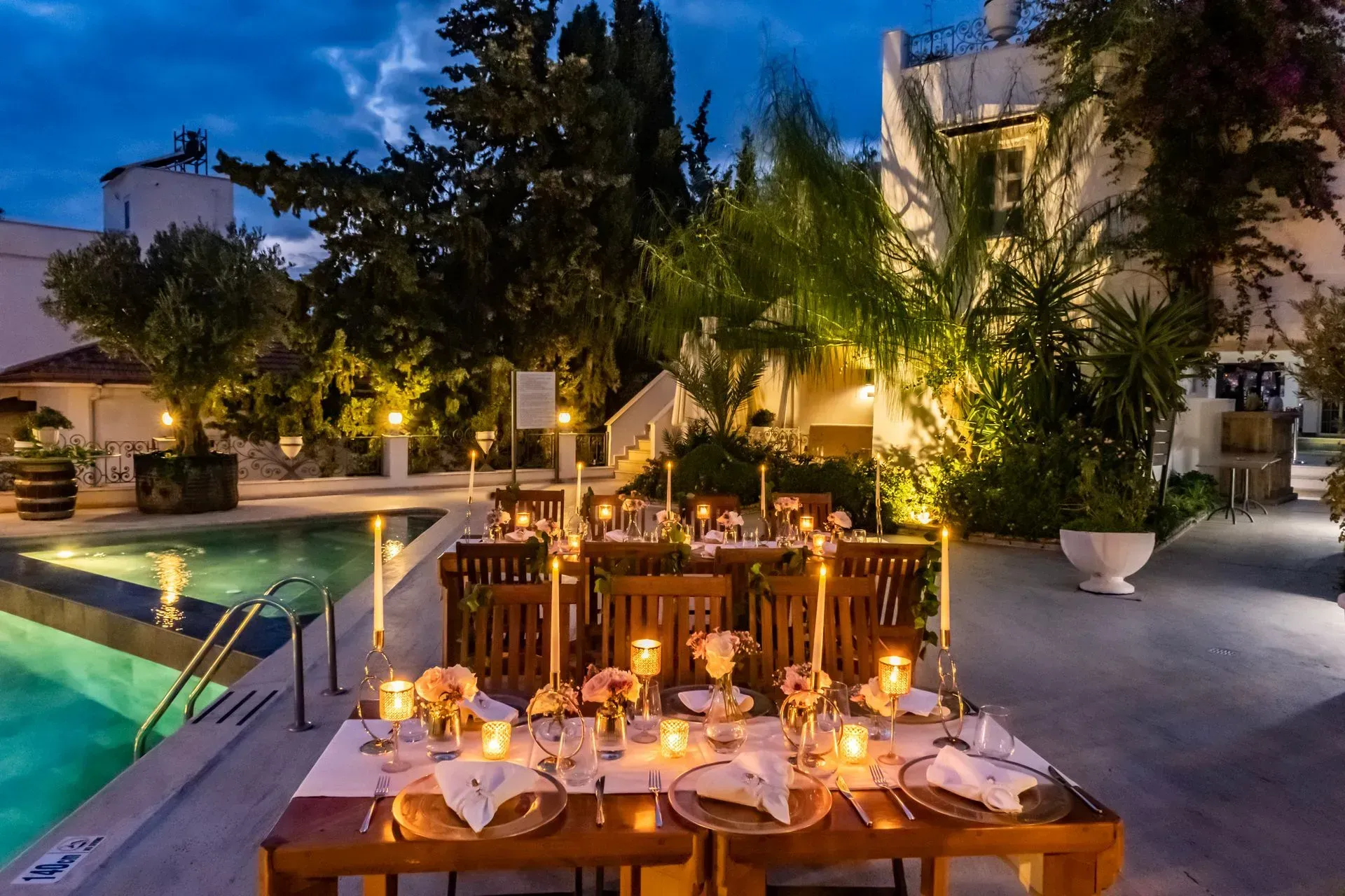 Manzara Boutique Hotel | Candlelit dinner table beside a pool at dusk, with warm lights and lush trees in a courtyard patio