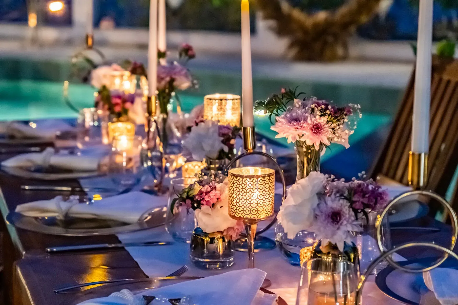 Manzara Boutique Hotel | Elegant outdoor dinner table with candles, purple flowers, and place settings by a pool at dusk