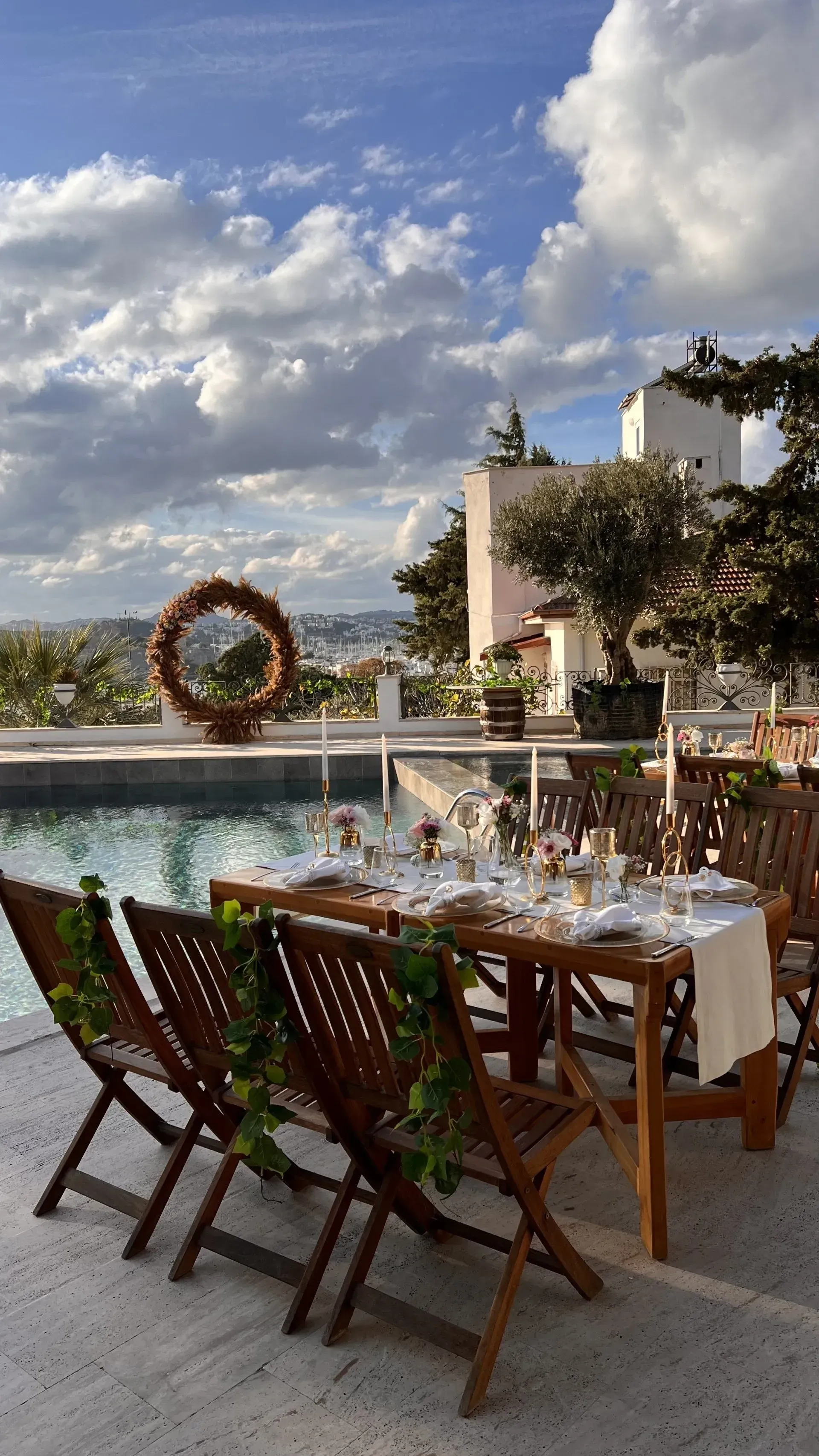 Manzara Boutique Hotel | Outdoor dining table by an infinity pool with a floral wreath and cloudy sky at sunset